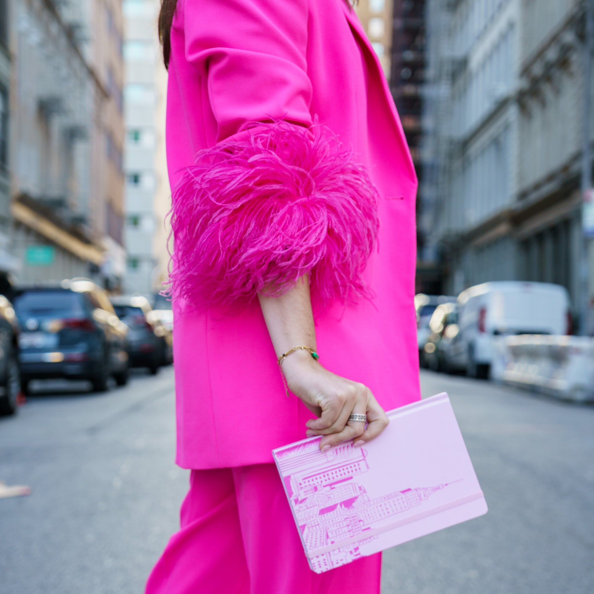 Person wearing a bright pink outfit with feathered sleeves on a city street.
