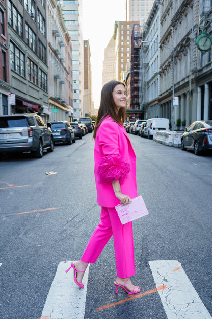 Woman in a bright pink outfit walking on a city street holding pink journal. 
