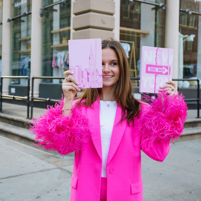 woman in pink suit holding two pink journals