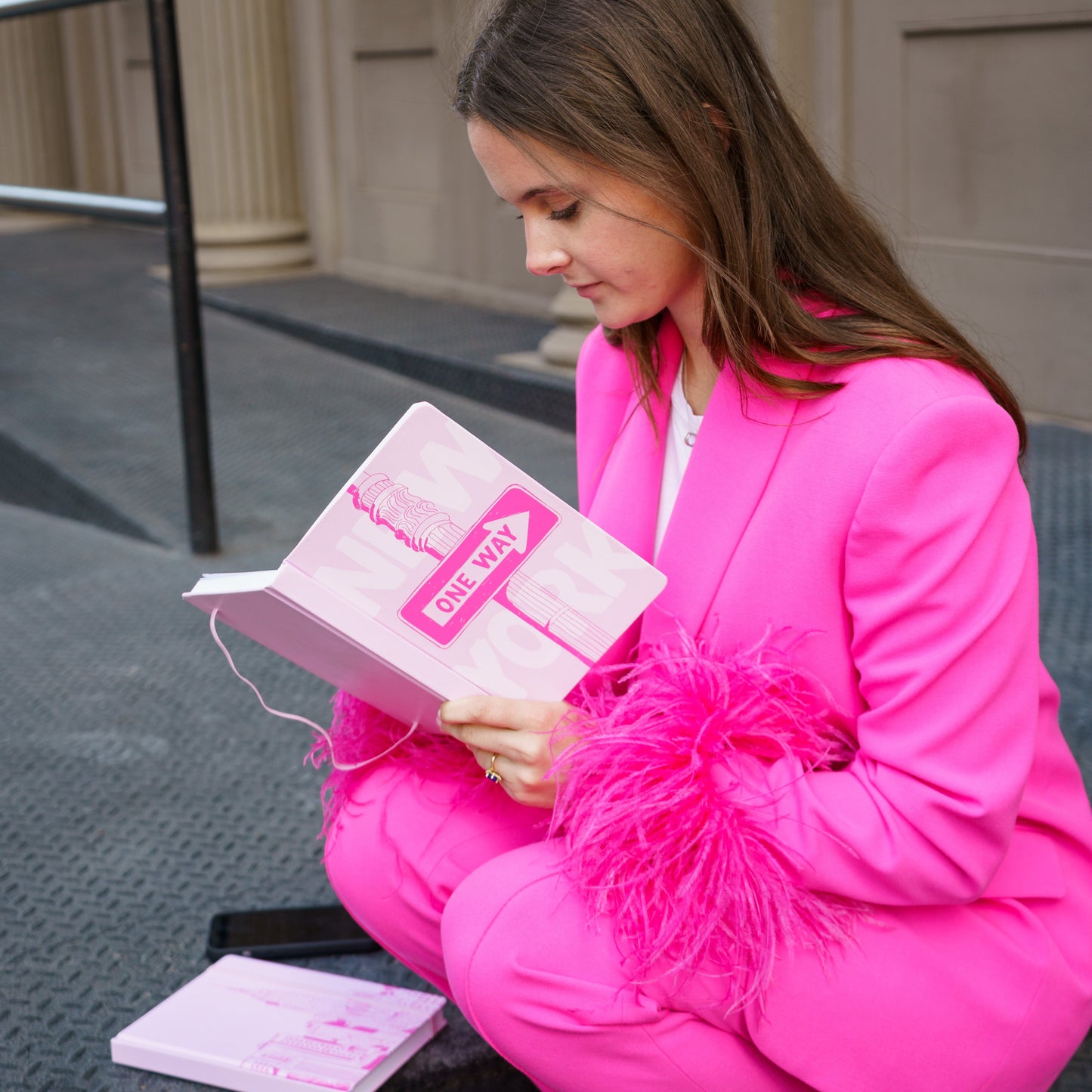 Person in a bright pink outfit sitting on a step, holding a pink book.