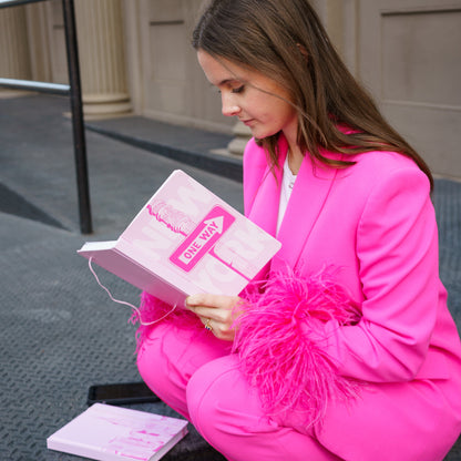 Person in a bright pink outfit sitting on a step, holding a pink book.